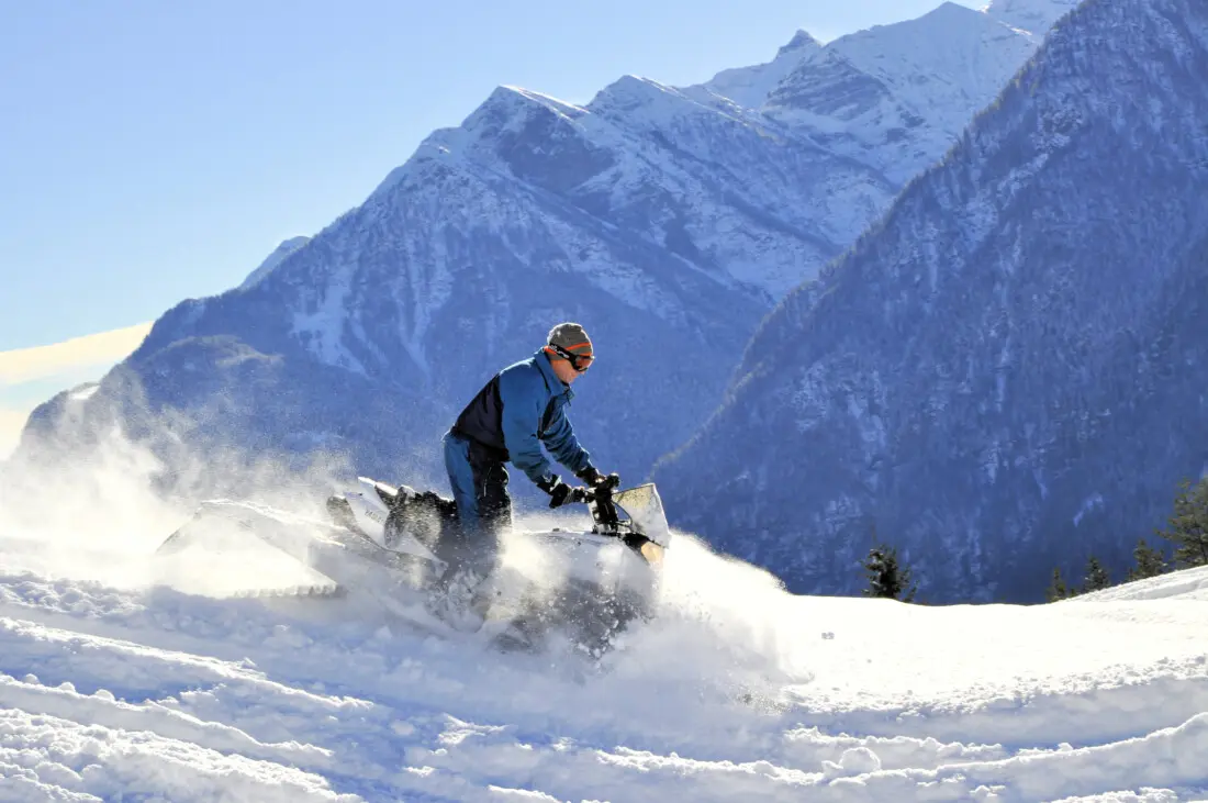 Snowmobil-Fahrer im Tiefschnee vor einem Bergpanorama